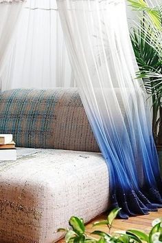 a couch with blue and white drapes on it in front of a potted plant