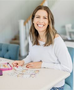 a smiling woman sitting at a table with some cards on the table and pencils in front of her