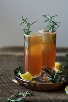 two glasses filled with lemonade and rosemary garnish on top of a wooden table