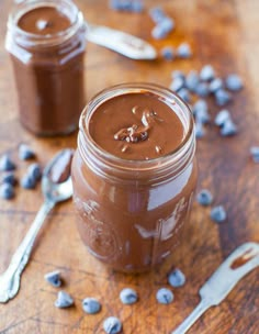 two jars filled with chocolate pudding sitting on top of a wooden table next to spoons