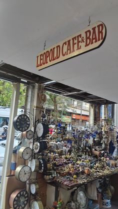 an outdoor market with many clocks and other items on the table, including a sign that reads leopold cafe - bar