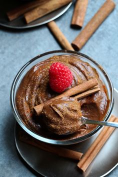 a glass bowl filled with chocolate pudding next to cinnamon sticks and a raspberry