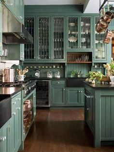 a kitchen with green cabinets and wooden floors, pots and pans hanging from the ceiling