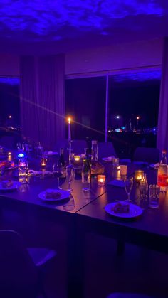 a long table with plates and glasses on it in front of a window at night