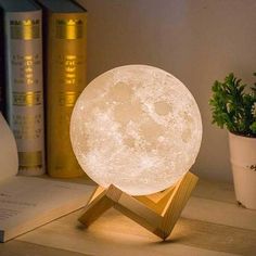 the moon lamp is sitting on top of a desk next to some books and a potted plant