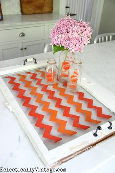 some vases with flowers in them sitting on a white table top and an orange chevroned tray