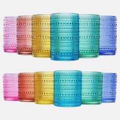 many different colored glass cups are lined up on a white surface, with one empty cup in the middle