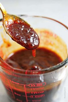 a spoon full of ketchup is being held up by a measuring cup filled with sauce