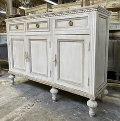 an old white cabinet with gold trimmings in a warehouse or shop, sitting on the floor