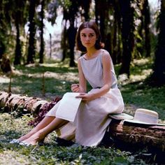 a woman sitting on top of a log in the woods wearing a dress and hat