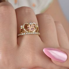 a woman's hand with a pink manicure holding a gold and diamond ring