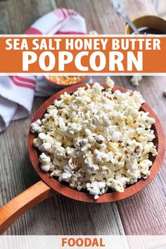 a wooden spoon filled with popcorn on top of a table next to a bowl of popcorn