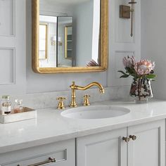 a bathroom sink with a large mirror above it and flowers in a vase on the counter