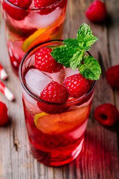 two glasses filled with ice and raspberries on top of a wooden table