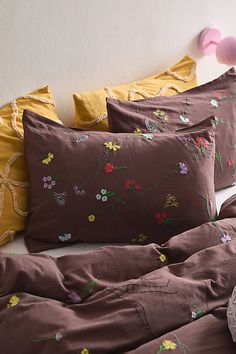 the bed is made with brown linens and colorful flowers on it, along with yellow pillows