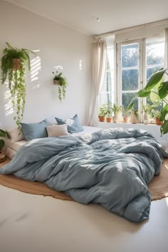 an unmade bed with blue sheets and pillows in a room filled with potted plants