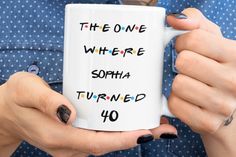 a woman holding a white coffee mug with the words,'the one where sophia turned 40 '