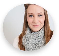 a woman with long hair wearing a gray cowl scarf and smiling at the camera