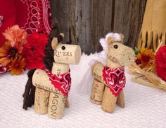 two wine cork horses are sitting next to each other on a table with flowers in the background