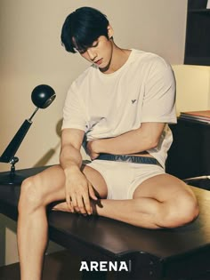 a young man sitting on top of a wooden table next to a desk with a lamp