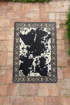 a black and white area rug sitting on top of a brick floor next to green plants