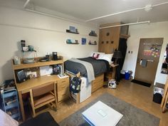 a dorm room with a bed, desk and refrigerator