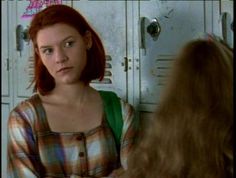 a woman standing in front of lockers looking at another person with red hair and green eyes