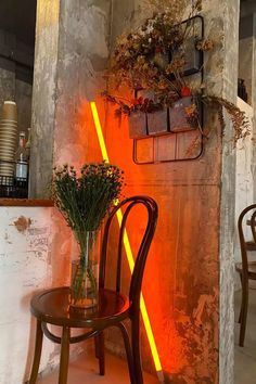 a chair sitting next to a table with flowers on it in front of a wall