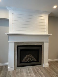 an empty fireplace with white paint and wood on the mantle, in a room with hard wood flooring