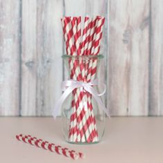 two red and white striped paper straws in a glass jar next to candy canes