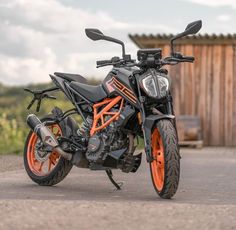 an orange and black motorcycle parked in front of a wooden building on the side of a road