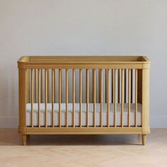 a small wooden crib with white sheets on the bottom and beige walls behind it