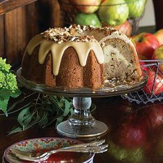 a bundt cake with icing and nuts is on a table next to some fruit