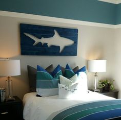 a bed with blue and white pillows on top of it next to a wall mounted shark