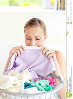 a woman sitting on a couch holding a laundry basket with clothes in it and covering her mouth