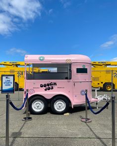 a pink food truck parked on top of a parking lot next to a yellow fence