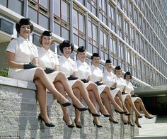 seven women in uniforms are sitting on the steps outside an office building and smiling at the camera