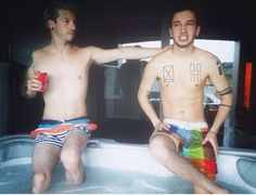 two men sitting in a hot tub with one holding a drink and the other wearing swim trunks