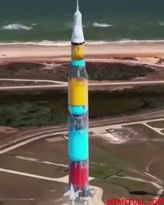 a multicolored rocket is shown in front of the ocean and sand area,