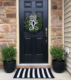 a black front door with a wreath and two potted plants