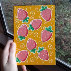 a hand holding up a small square painted with strawberries on yellow and pink background