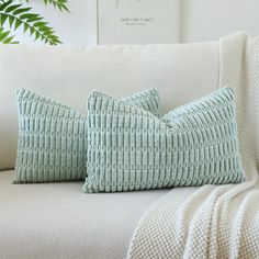 two green pillows sitting on top of a white couch next to a potted plant