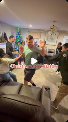 a group of people dancing in a living room with a christmas tree on the wall