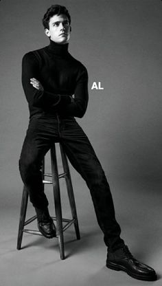 a man sitting on top of a stool wearing a turtle neck sweater and black pants