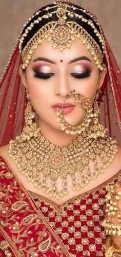 a woman wearing a red bridal outfit with gold jewelry on her face and nose