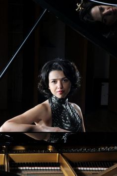 a woman sitting at a piano with her hands on the keyboard and looking into the camera