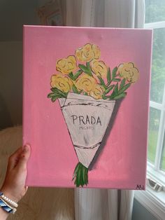 a person holding up a pink painting with yellow flowers in the shape of a vase