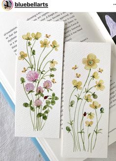 three cards with watercolor flowers on them sitting on top of an open book next to each other