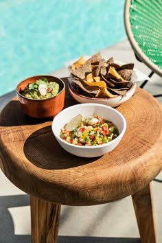 two bowls of salsa and tortilla chips on a table next to a pool