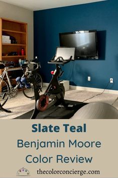 a room with blue walls and an exercise bike in the foreground, there is a flat screen tv on the wall